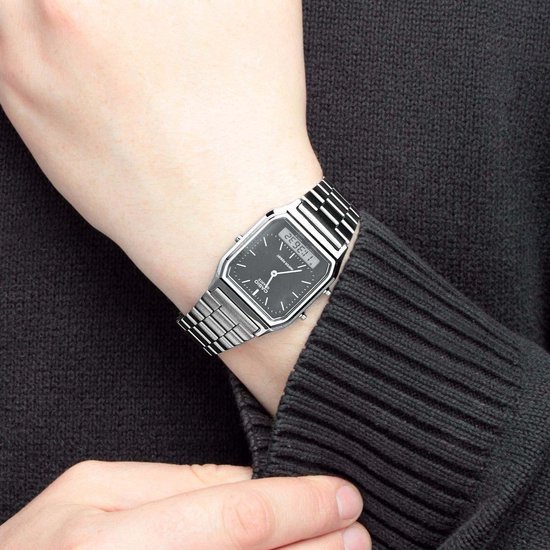 Poignet portant une montre argentée avec bracelet métallique, cadran noir, heure analogique et numérique, avec un cardigan noir en tricot.