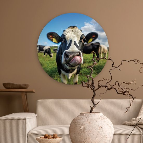 Ronde muurdecoratie met een koe die met haar tong likt, geplaatst in een woonkamer boven een bank.