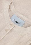 Close-up van de kraag en knoopjes van een beige linnen blouse met Minus-label.