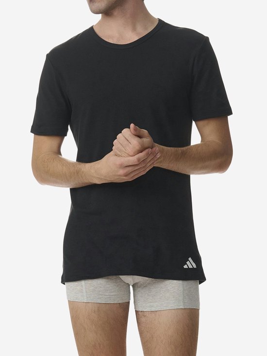 Man in zwart Adidas T-shirt en grijze boxershort, met handen ineengestrengeld.