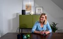 Zwarte Harman Kardon speaker op een groene kast, met een vrouw die op haar telefoon kijkt.