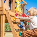 Jongen klimt op een houten speeltoestel met kleurrijke klimstenen.