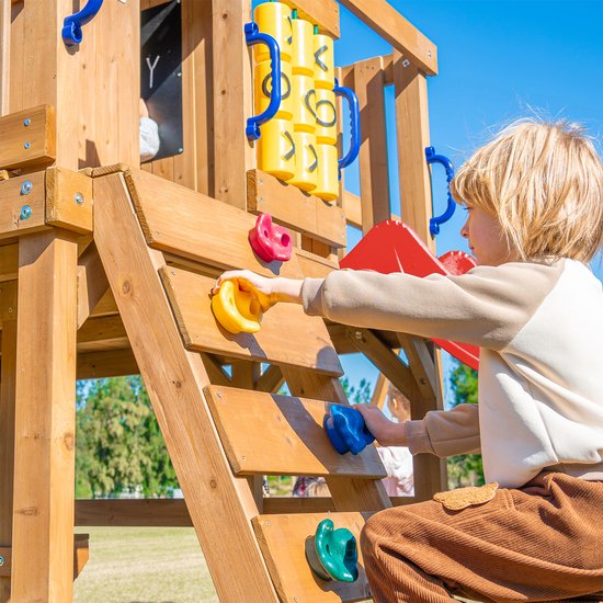 Jongen klimt op een houten speeltoestel met kleurrijke klimstenen.