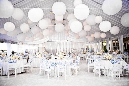 Trouwlocatie versierd met vele witte papieren lampionnen en gedekte tafels.