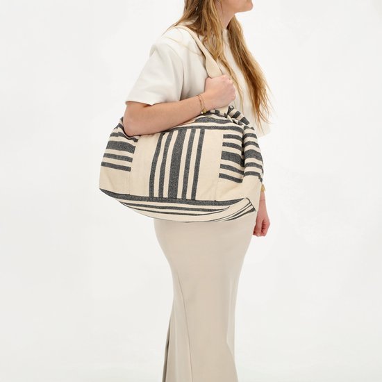 Vrouw met lange beige rok en wit T-shirt draagt een grote beige tas met zwart gestreepte patronen.