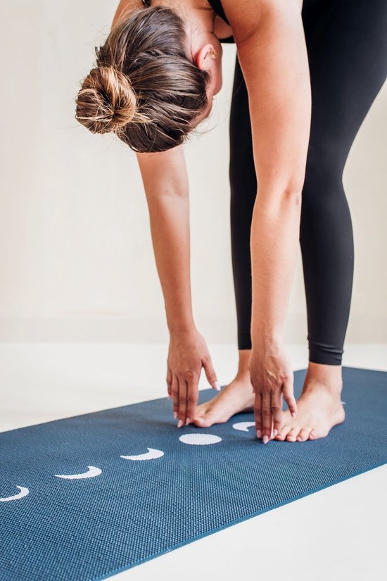 Vrouw in zwarte sportkleding buigt voorover op een blauwe yogamat met maanfasen.