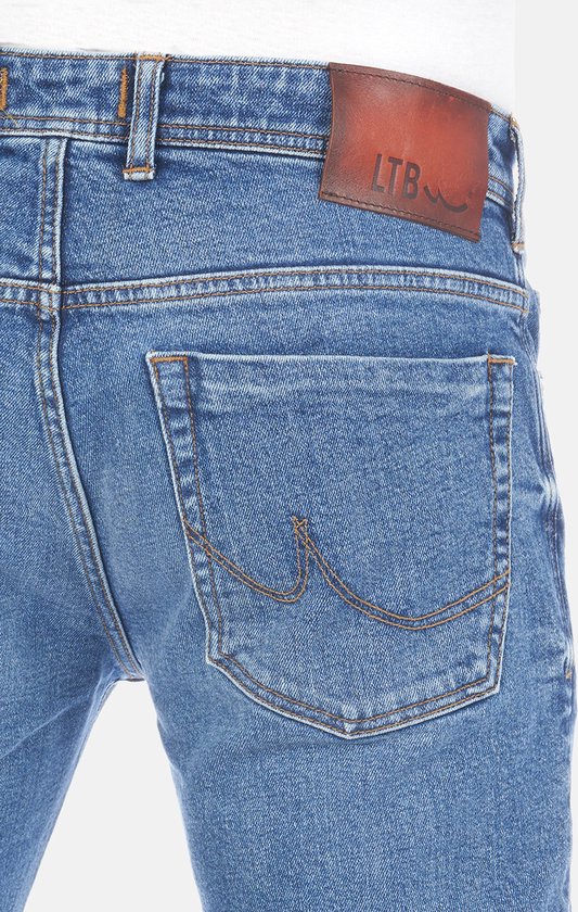 Detail van de achterkant van een spijkerbroek, medium blauwe denim met stonewash effect, achterzak met sierstiksels en een bruin leren label.