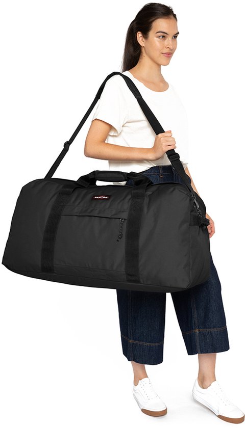 Vrouw met een zwarte Eastpak reistas over de schouder, gedragen bij de hand.