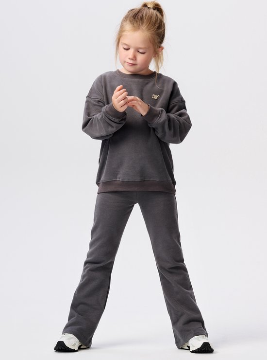 Meisje in donkergrijs joggingpak met ronde hals en wijduitlopende broekspijpen.