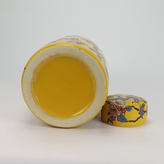 Onderkant van een gele pot met bloemendecoratie, met het deksel ernaast.