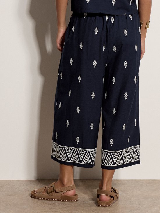 Achterkant van marineblauwe culotte met witte diamantjes en geborduurde randen, gedragen met sandalen.