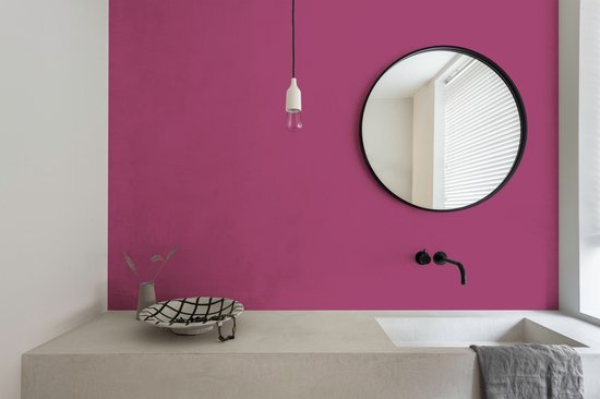 Een badkamermeubel met een fuchsia muur en zwarte spiegel.