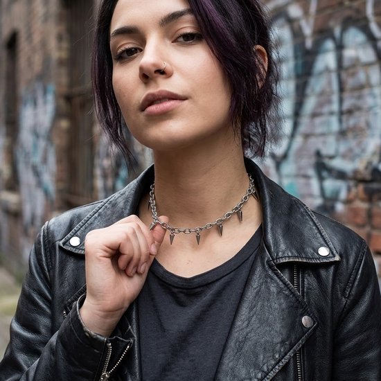 Model met kort paars haar draagt een zilverkleurige schakelketting choker met puntige spikes over een zwart T-shirt en leren jas.