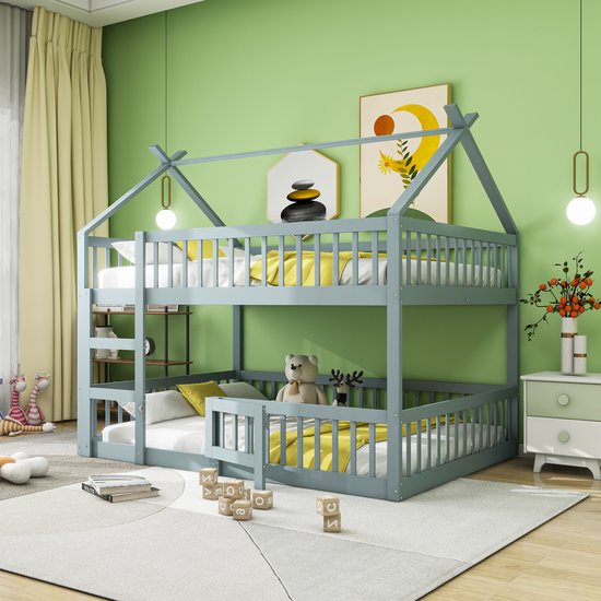 Grijs houten stapelbed met een huisvormig dak, gele dekens, witte lakens en knuffels.