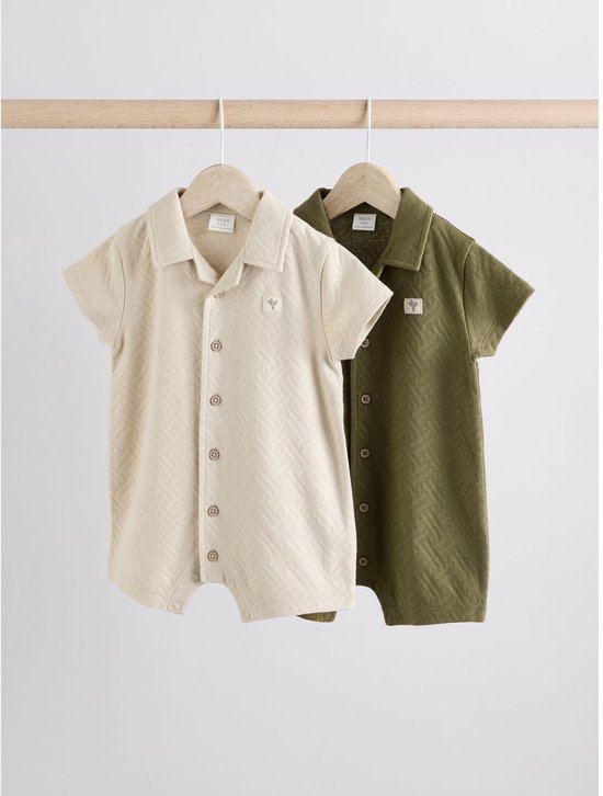 Twee babyrompertjes, beige en groen, met visgraatpatroon, hangend aan een houten rek.
