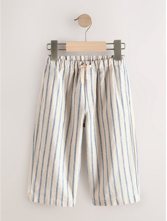 Crème broek met verticale blauwe strepen en een trekkoord, hangend aan een kledinghanger.