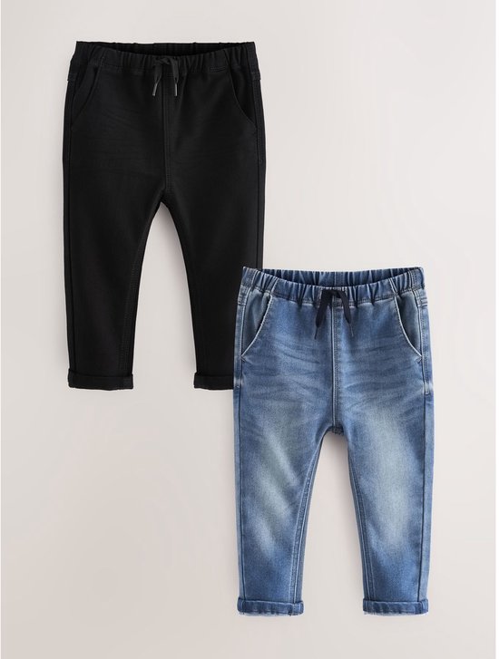 Set van twee kinderbroeken, een in denimblauw en een in zwart, naast elkaar. Beide hebben een elastische tailleband met koordje en opgerolde zomen.
