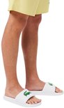 Witte Lacoste badslippers met groene krokodil op de band. Gedragen door een model met gele shorts.