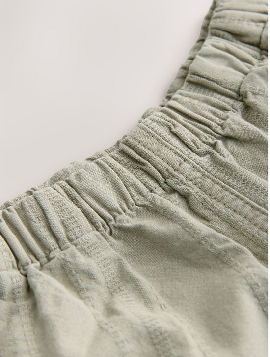 Detail van de elastische tailleband van een lichtgroene broek met verticale textuur.