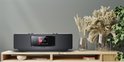 Zwarte Kenwood radio op een houten meubel, naast decoratieve vazen met droogbloemen.