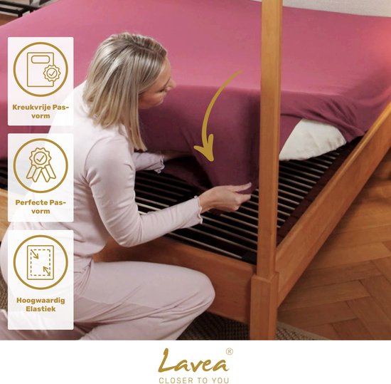 Een vrouw bevestigt een koraalkleurig hoeslaken met perfecte pasvorm aan een bed met lattenbodem.