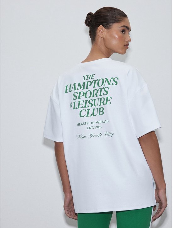 Model draagt een wit T-shirt met groene tekst op de rug en groene sportlegging.