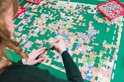 Vrouw met krullend bruin haar legt puzzelstukjes op een groene puzzelmat.