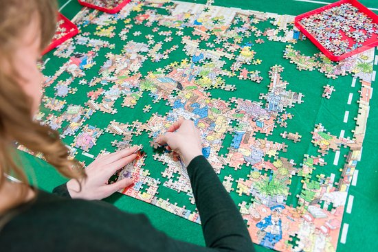 Vrouw met krullend bruin haar legt puzzelstukjes op een groene puzzelmat.