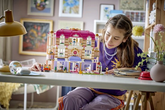 Meisje bouwt aan LEGO Friends Heartlake City Grand Hotel, een paars-wit gebouw met poppetjes en dieren.