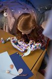 Een meisje met rood haar bouwt met LEGO's op een tafel, met een paars en wit trouwboot-bouwpakket.