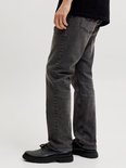 Zijaanzicht van een man die donkergrijze jeans draagt met zwarte schoenen.