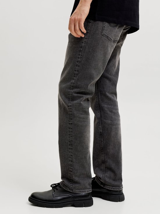 Zijaanzicht van een man die donkergrijze jeans draagt met zwarte schoenen.