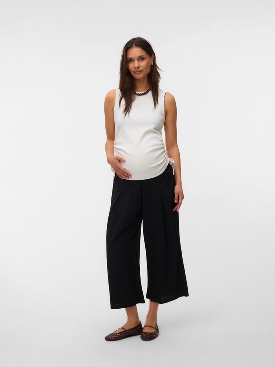 Zwangere vrouw in witte top met ruches en zwarte, wijde, cropped zwangerschapsbroek.