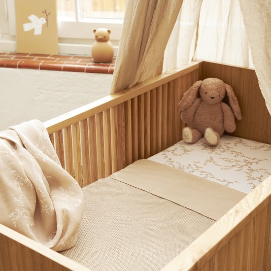 Houten wieg met een bruine konijnenknuffel en een deken met bladerpatroon.