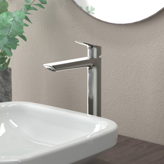 Hoge chromen wastafelkraan boven een witte wasbak, in een moderne badkamer met een spiegel en planten.