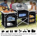 Campingkeuken met aanrechtbladen, gasbrander, waterkoker, pizza, geroosterde kip, fruit, groenten en kookgerei.