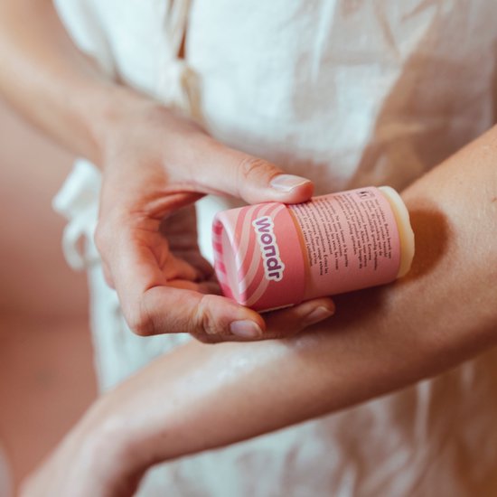 Des mains appliquent le bâton de beurre corporel à l'abricot Wondr sur le bras.