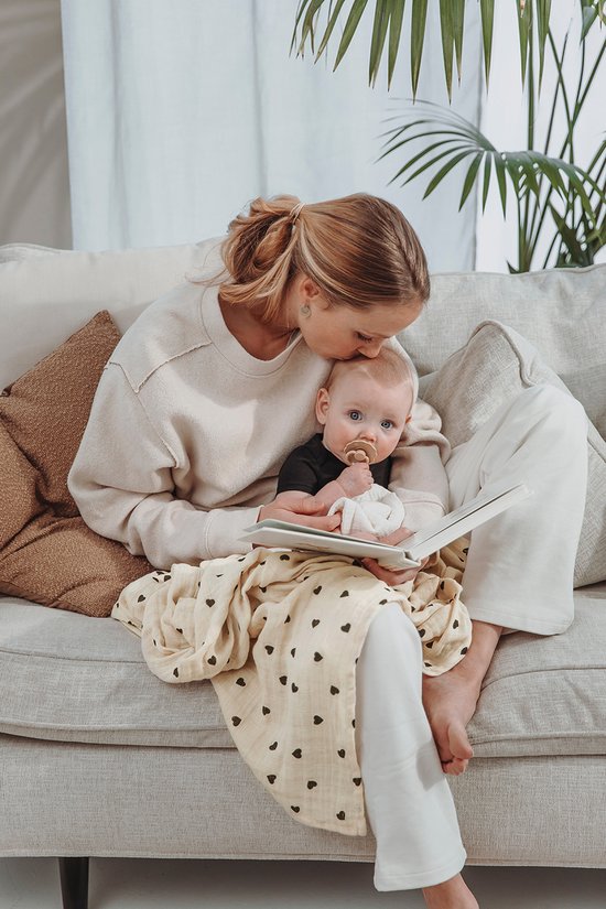 Vrouw kust baby op voorhoofd terwijl ze samen een boek lezen op de bank.