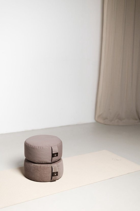 Twee ronde meditatiekussens, één taupe en één donkerder taupe, gestapeld op een beige yogamat.