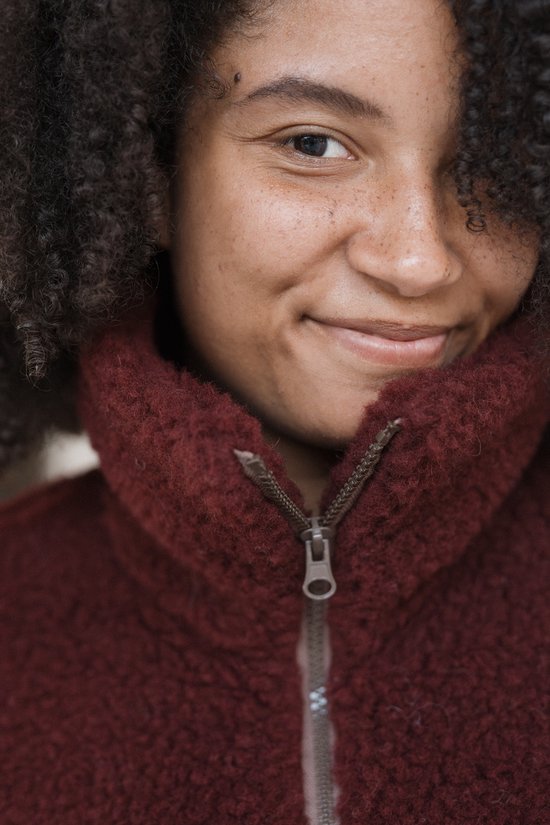 Close-up van een model in een bordeauxrode wollen bodywarmer met ritssluiting.