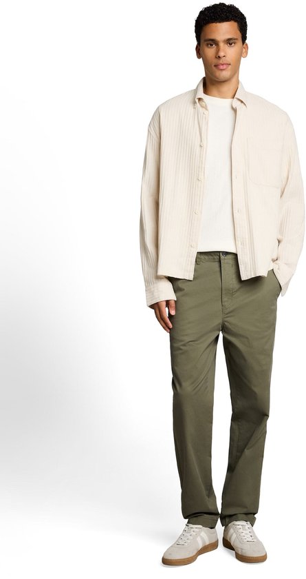 Man met een crème ribgebreide openvallende blouse over een wit T-shirt en olijfgroene chino. Casual sneakers.