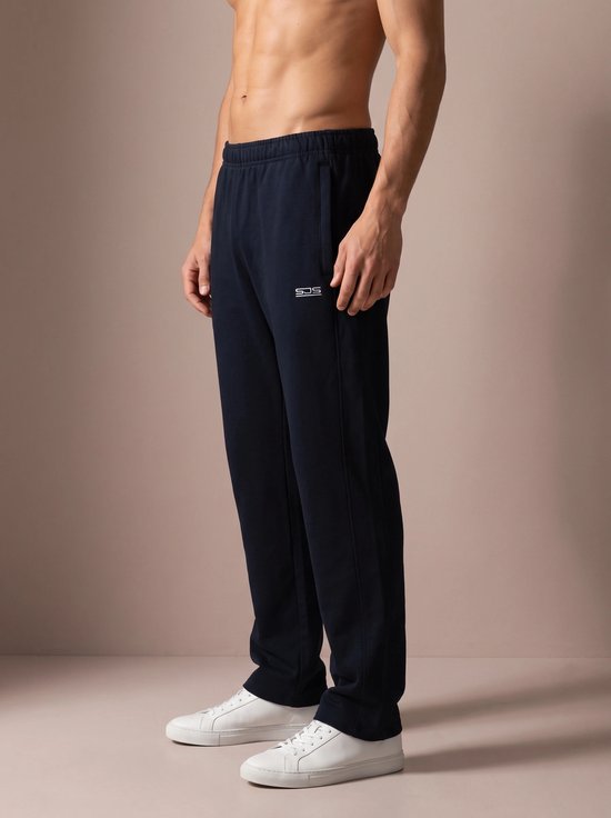 Homme de profil portant un pantalon de sport bleu marine avec logo, baskets blanches.