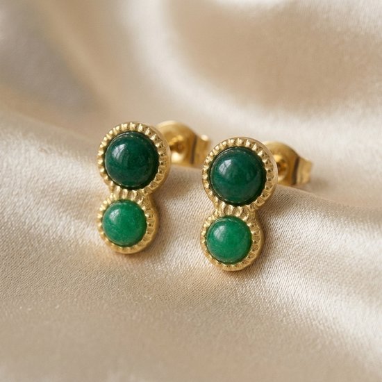 Gouden oorknopjes met dubbele ronde groene stenen op een crèmekleurige satijnen achtergrond.