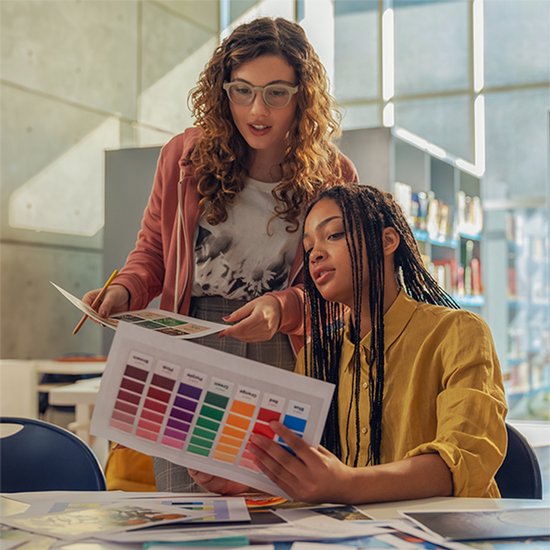 Twee vrouwen bekijken een kleurenwaaier tijdens het werken met creatieve ontwerpen.