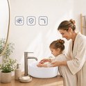 Moeder en kind wassen hun handen in een witte opbouwwaskom in een lichte badkamer.