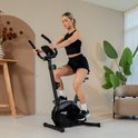 Zwarte hometrainer met een vrouw in sportkleding die erop zit.