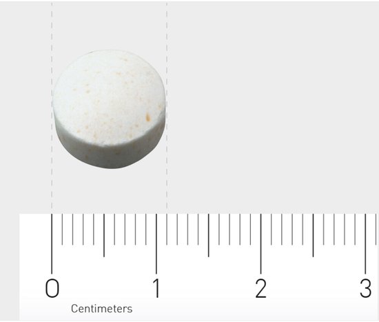 Een ronde, witte kauwtablet met bruine spikkels, gepresenteerd naast een centimeter schaal.