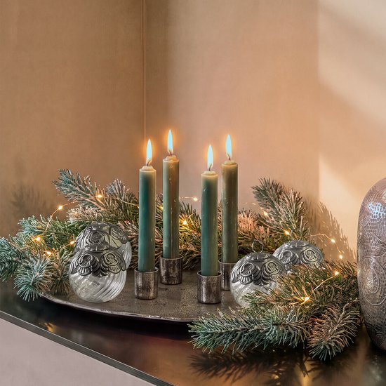 Vier brandende groene kaarsen in antiekzilveren houders op een plateau met kersttakken en glazen bollen.