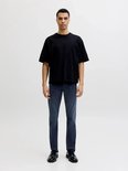 Man met donkere huid, met korte zwarte T-shirt en donkerblauwe jeans.
