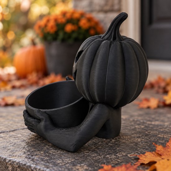 Zwarte pompoenschaal met griezelgezicht, staand op een veranda met herfstbladeren, een hand pakt een snoepje.